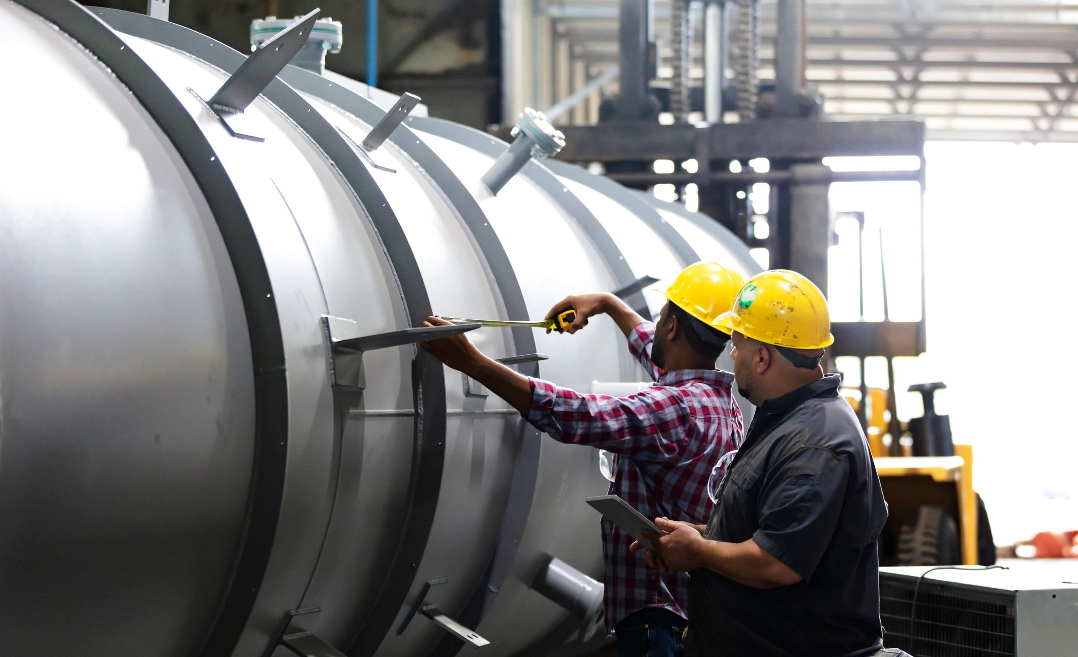 Two fabrication shop workers measuring a steel component